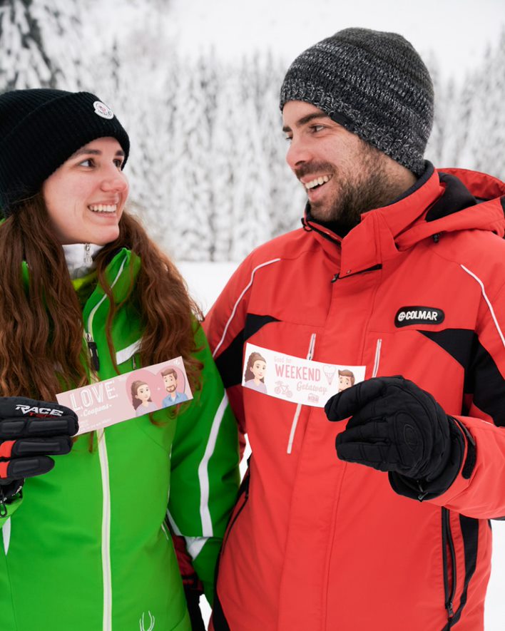 A couple in the snow holding Hooray Heroes personalized love coupons.