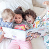 Three siblings are reading their personalized book for a family of five and laughing.