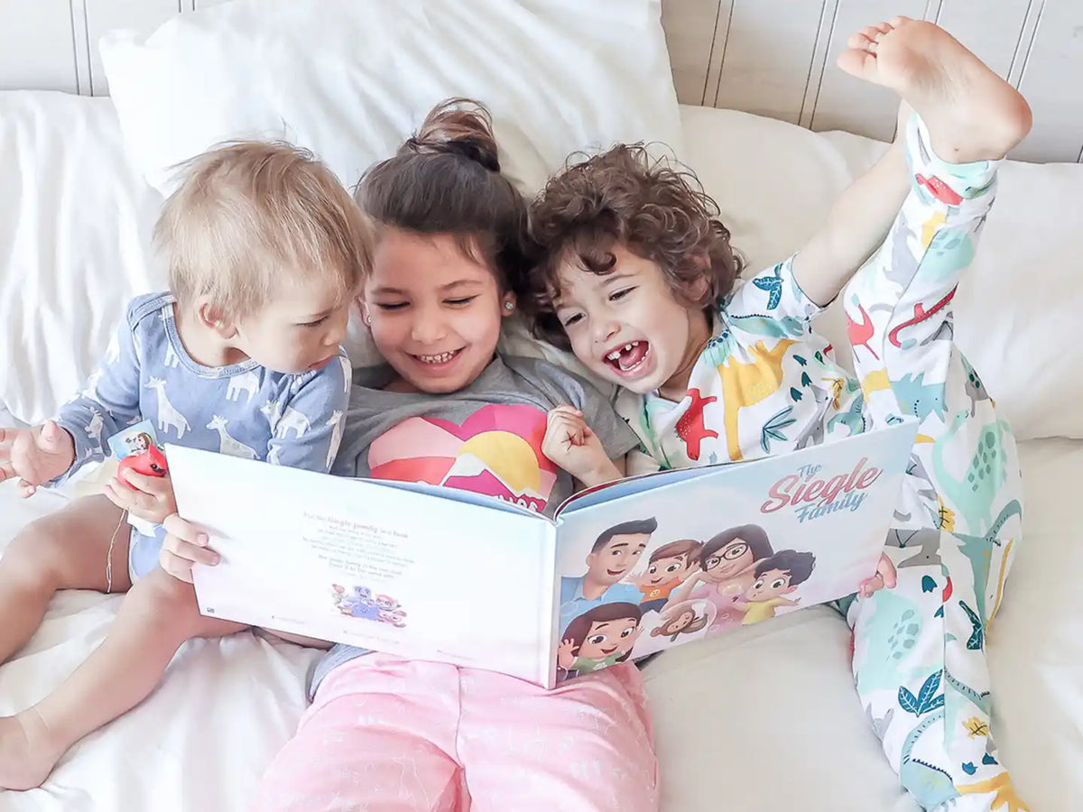 Three siblings are reading their personalized book for a family of five and laughing.