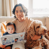 Man lovingly holding his little son and their dog reading an emotional book about what his son is going to be when he grows up.