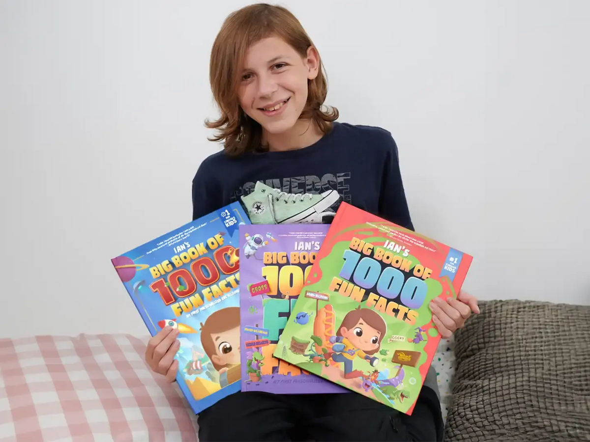 A boy is holding three different covers of personalized book of fun facts which are more fun than book of records.