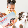 Little girl smiling at illustrations of her new personalized book made just for her and her pet dog Mochi.
