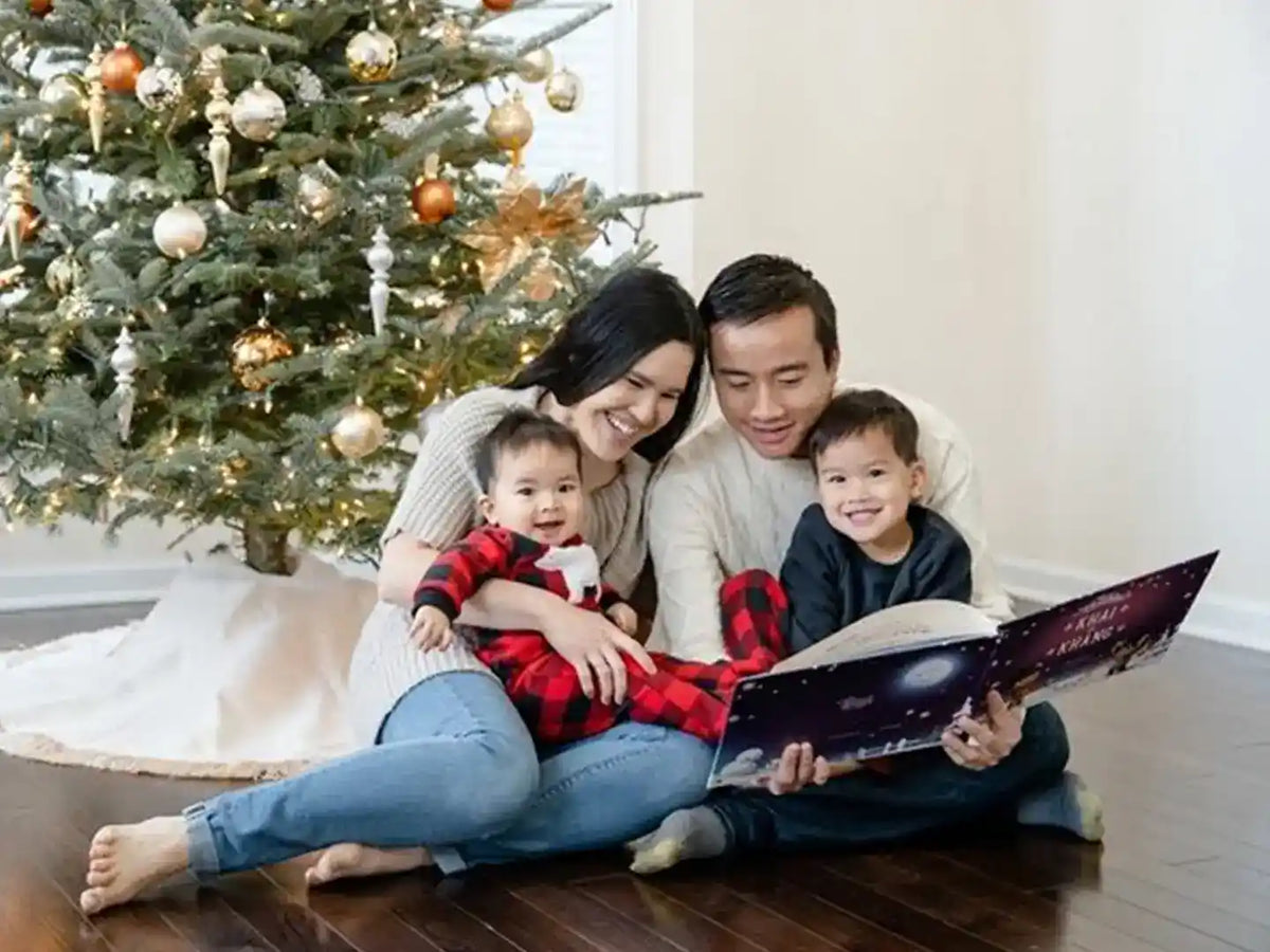 A happy family is reading the personalized book for siblings with their two kids beside the Christmas tree.