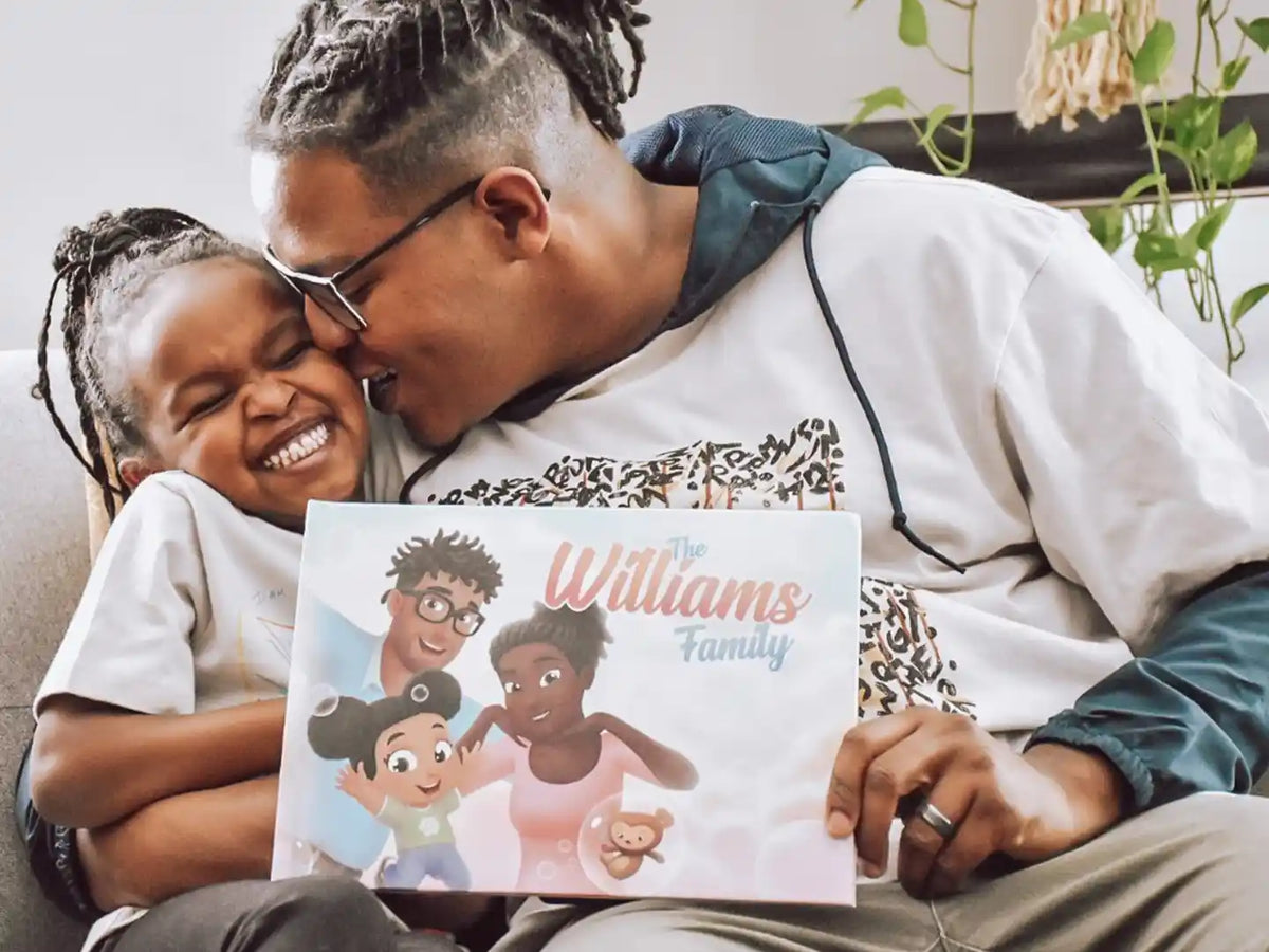 Dad giving a kiss to his daughter and holding their personalized book for families.