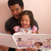 Girl is smiling while her dad is reading from a custom book they got for Christmas.