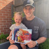 A smiling dad and toddler hold their customized “Days of You Being My Dada” book, the perfect personalized Father’s Day gift from a daughter.