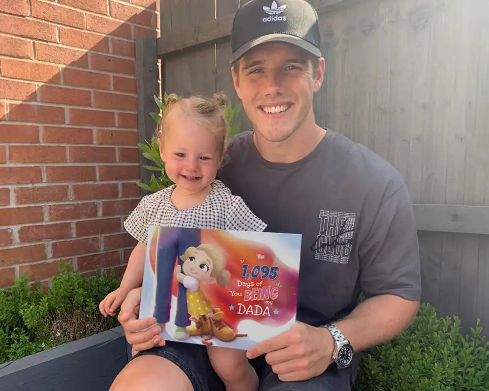 A smiling dad and toddler hold their customized “Days of You Being My Dada” book, the perfect personalized Father’s Day gift from a daughter.