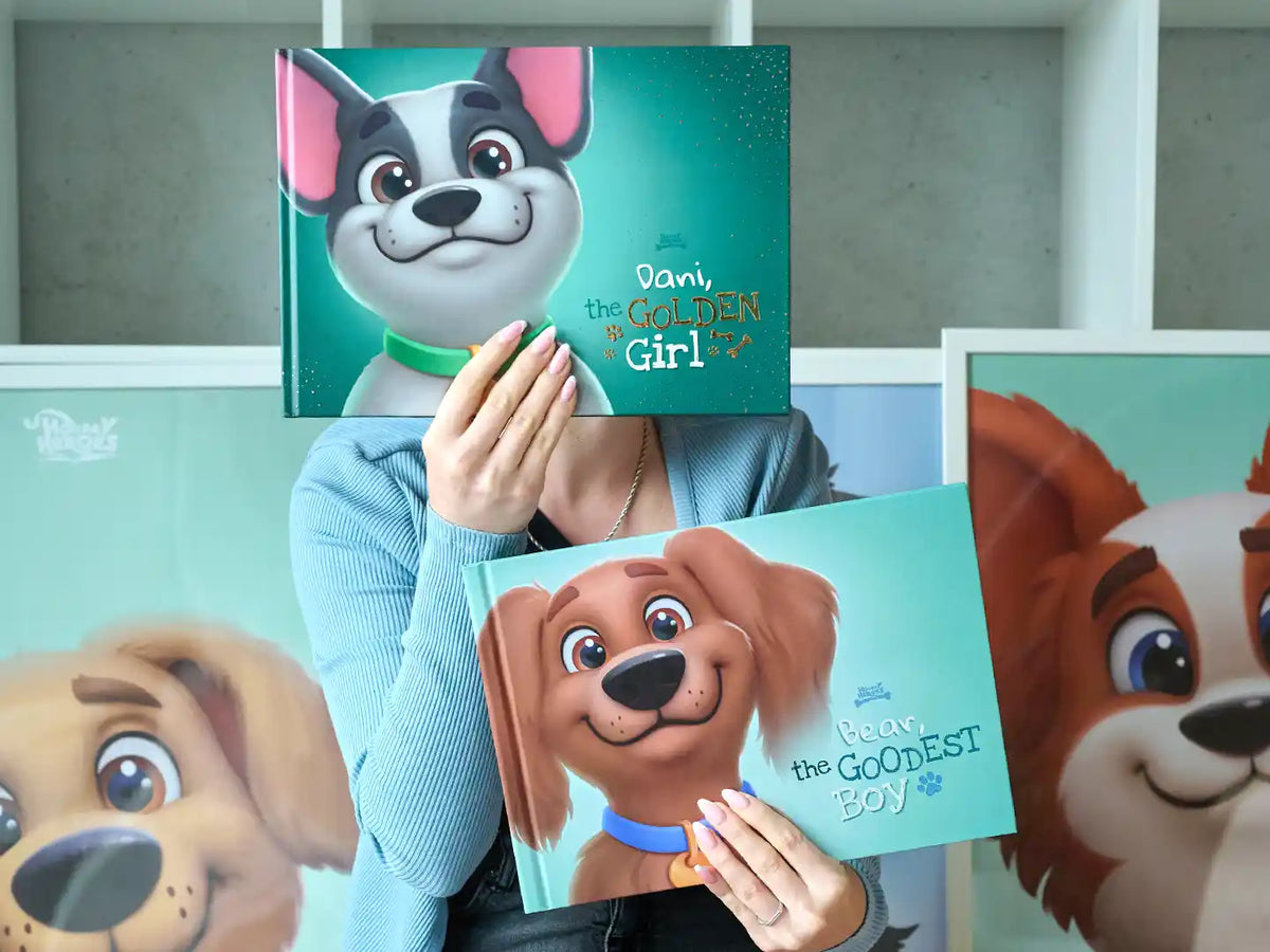 Person playfully holding two personalized dog books — 'Dani the Golden Girl' (premium version) and 'Bear the Goodest Boy' (basic version) — with large matching pet illustrations displayed in the background