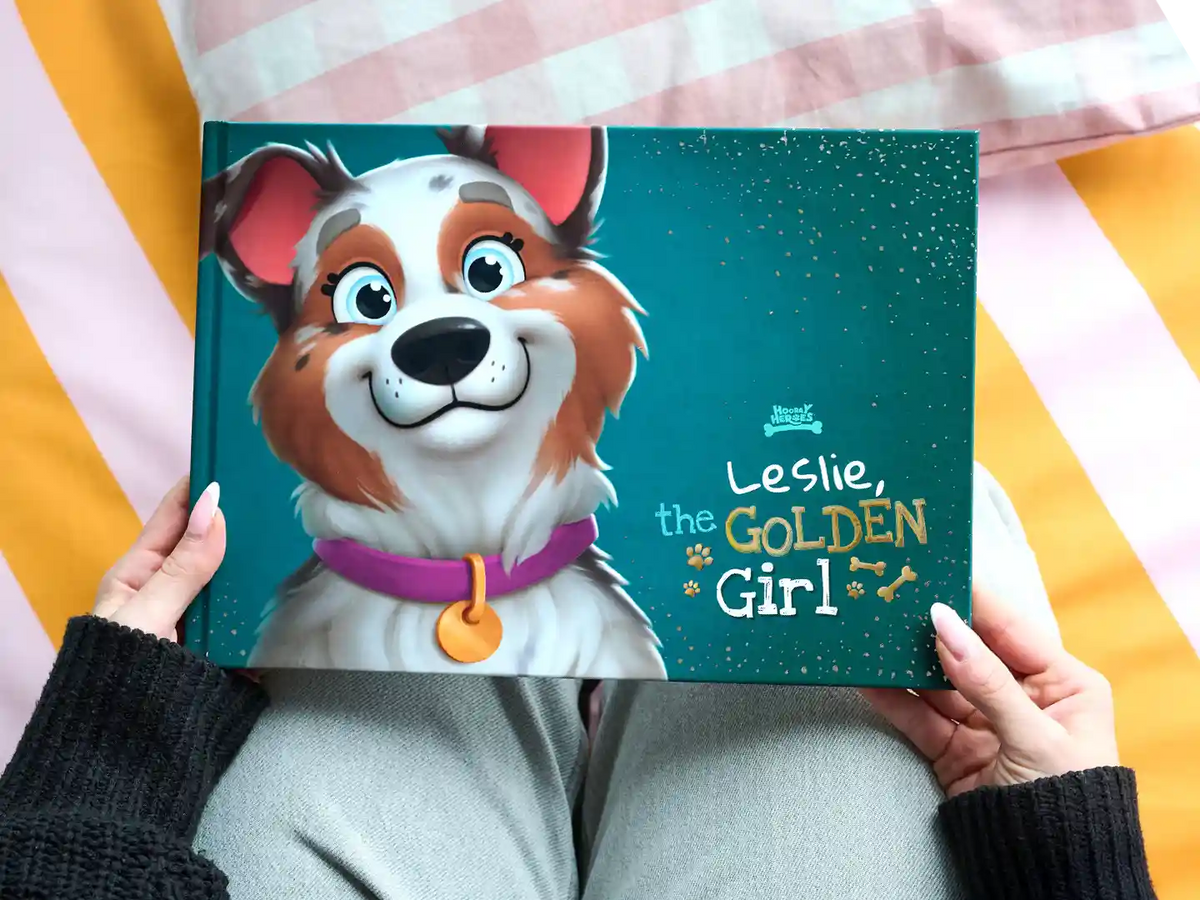 Person holding a premium personalized dog book titled 'Leslie, the Golden Girl,' featuring a happy cartoon dog.