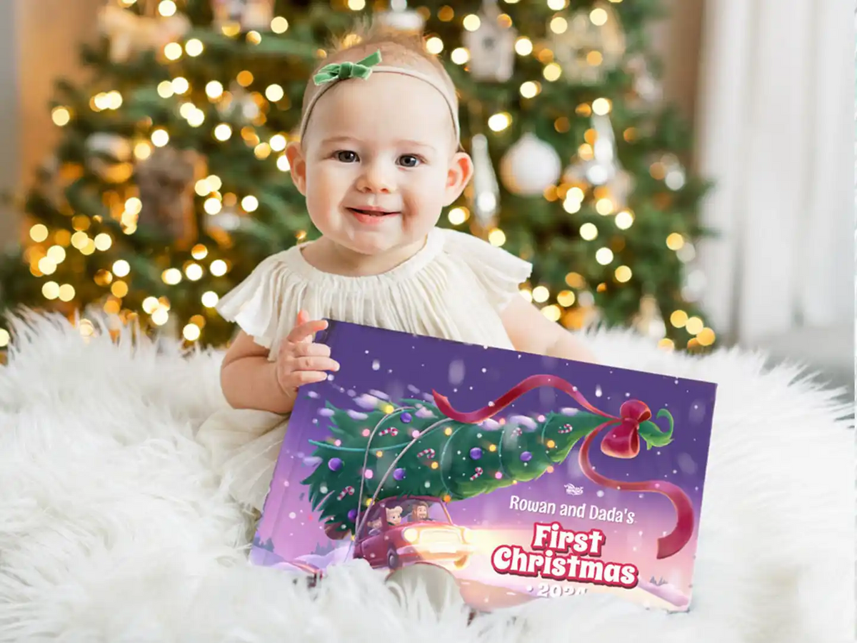 Baby holding a personalized Christmas gift book titled “Rowan and Dada’s First Christmas 2025.”